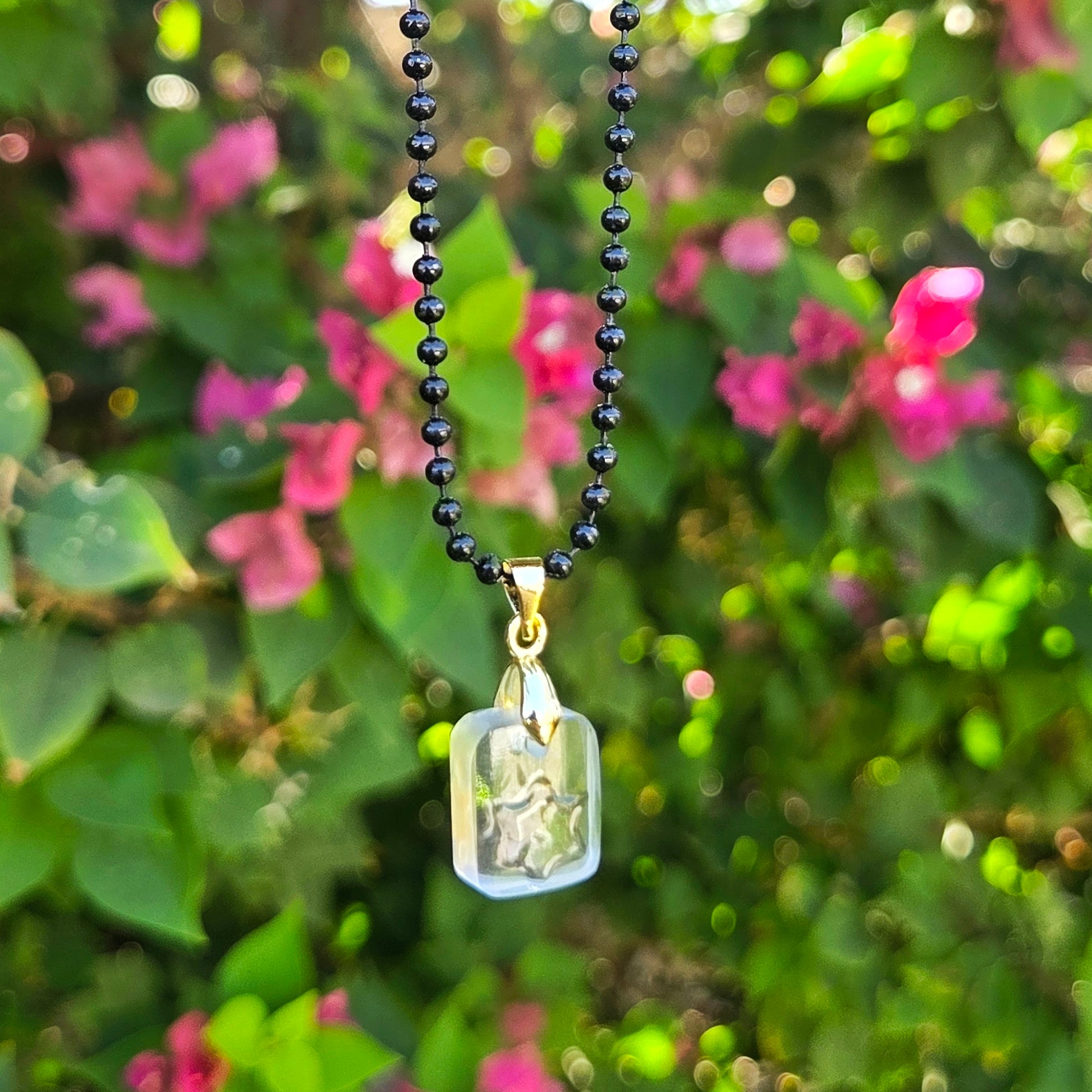 Necklace with a clear glass pendant with raised star hanging against a blurred natural background with pink flowers.