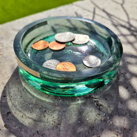 Green cut glass tray with coins on a concrete surface