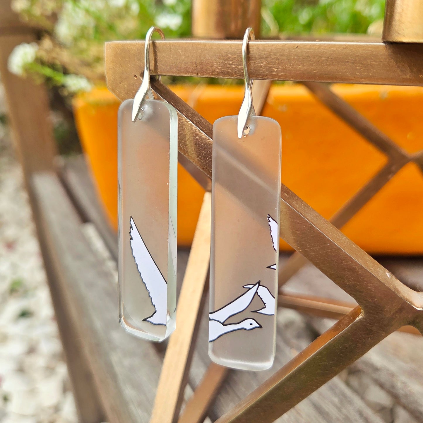 Transparent glass earrings with bird designs hanging on a metal rack.