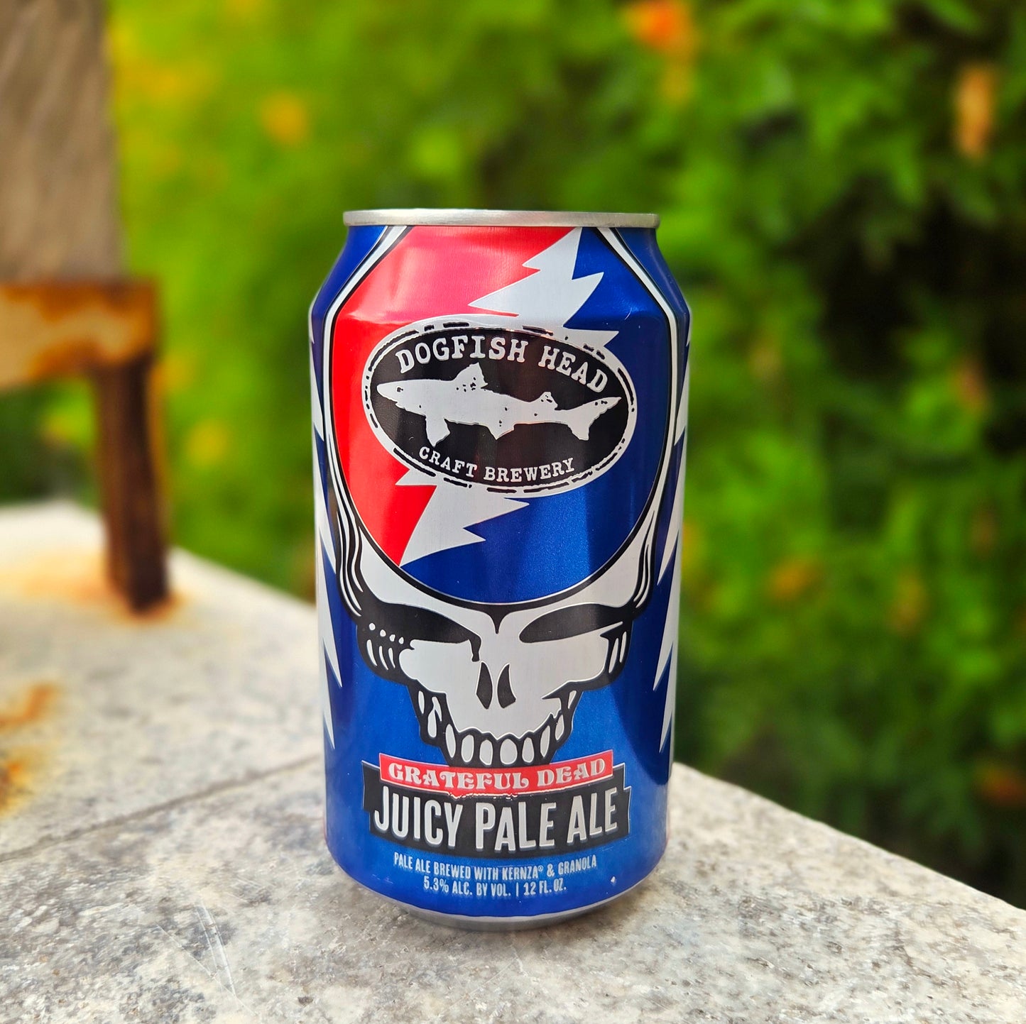 Front view of a recycled Dogfish Head beer can candle featuring the iconic Grateful Dead skull with a lightning bolt and bold blue and red design. Eco-friendly candle wax fills the can with a wooden wick peeking out the top.