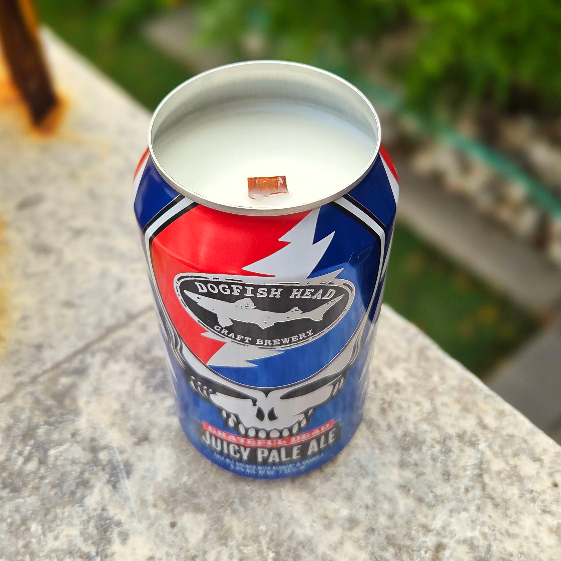 Angled photo of a handmade candle poured into a Grateful Dead-themed Dogfish Head beer can. The wooden wick and smooth soy wax surface are visible, framed by the can’s bold lightning bolt design.