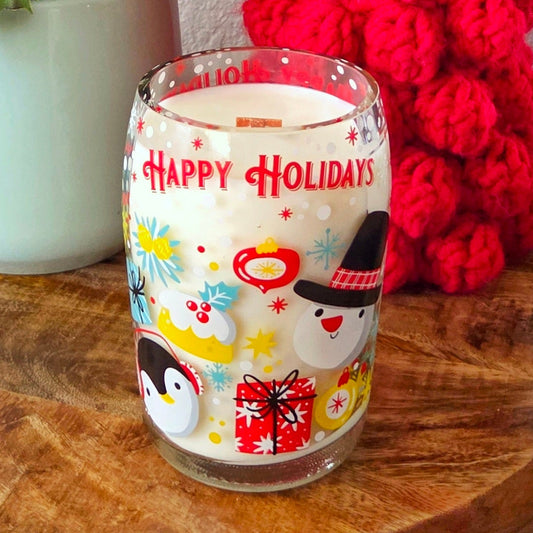 Decorative glass with 'Happy Holidays' text on a wooden surface with a plant and red knitted item in the background.