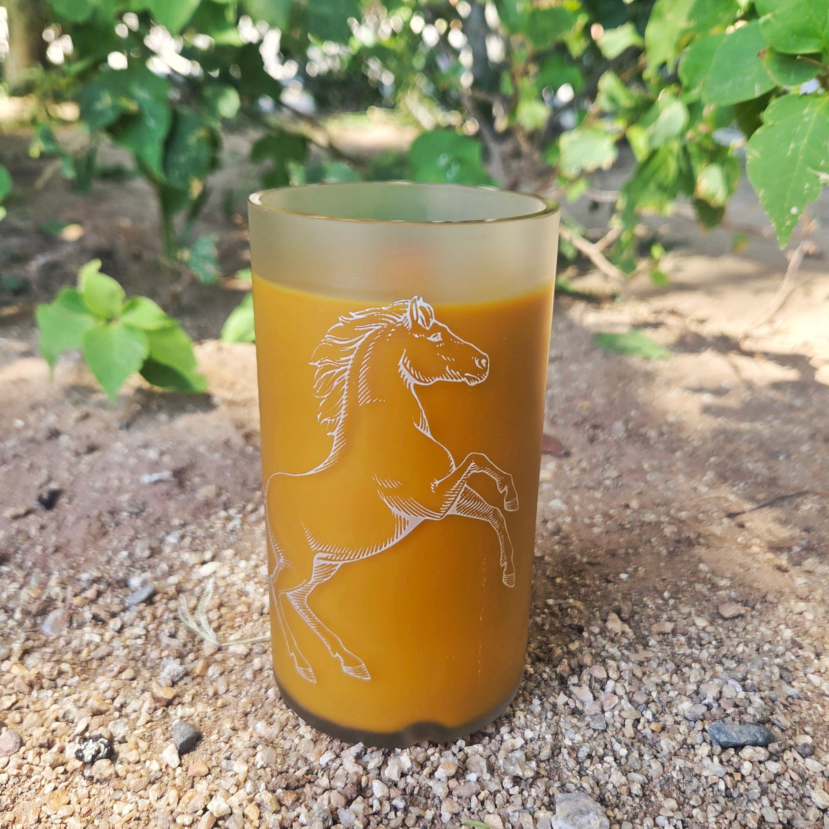 brownish yellow candle in a matte glass cut vodka bottle with horse design.