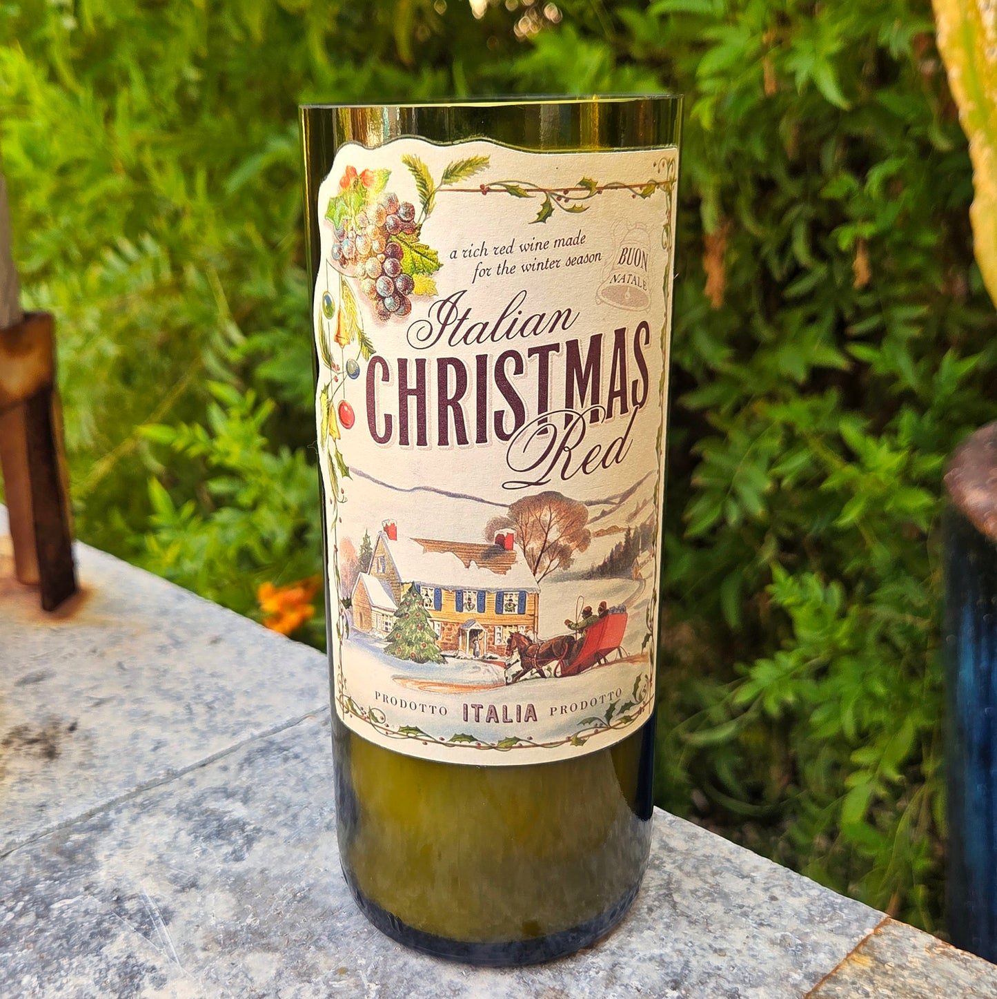 Wine bottle candle labeled 'Italian Christmas Red' on a stone surface with greenery in the background