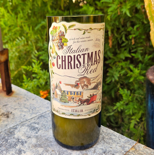 Wine bottle candle labeled 'Italian Christmas Red' on a stone surface with greenery in the background