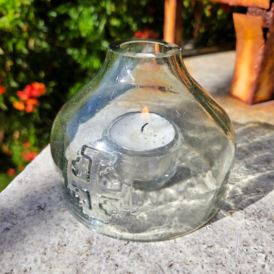 Clear glass lantern with a Jersaulem cross and a tea candle inside on a stone surface outdoors.