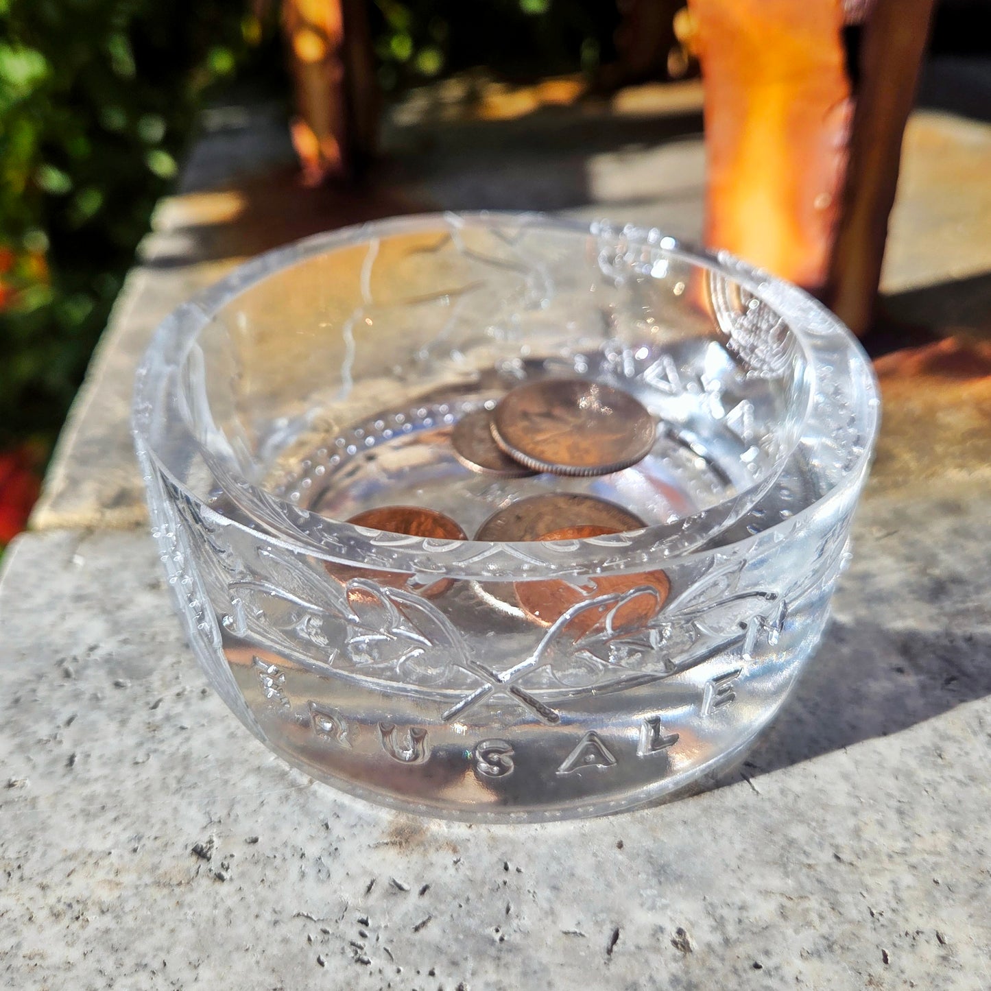 Clear glass bowl with coins on a stone surface