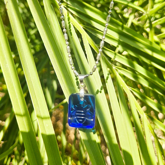 Blue glass pendant necklace on a chain against a green leafy background
