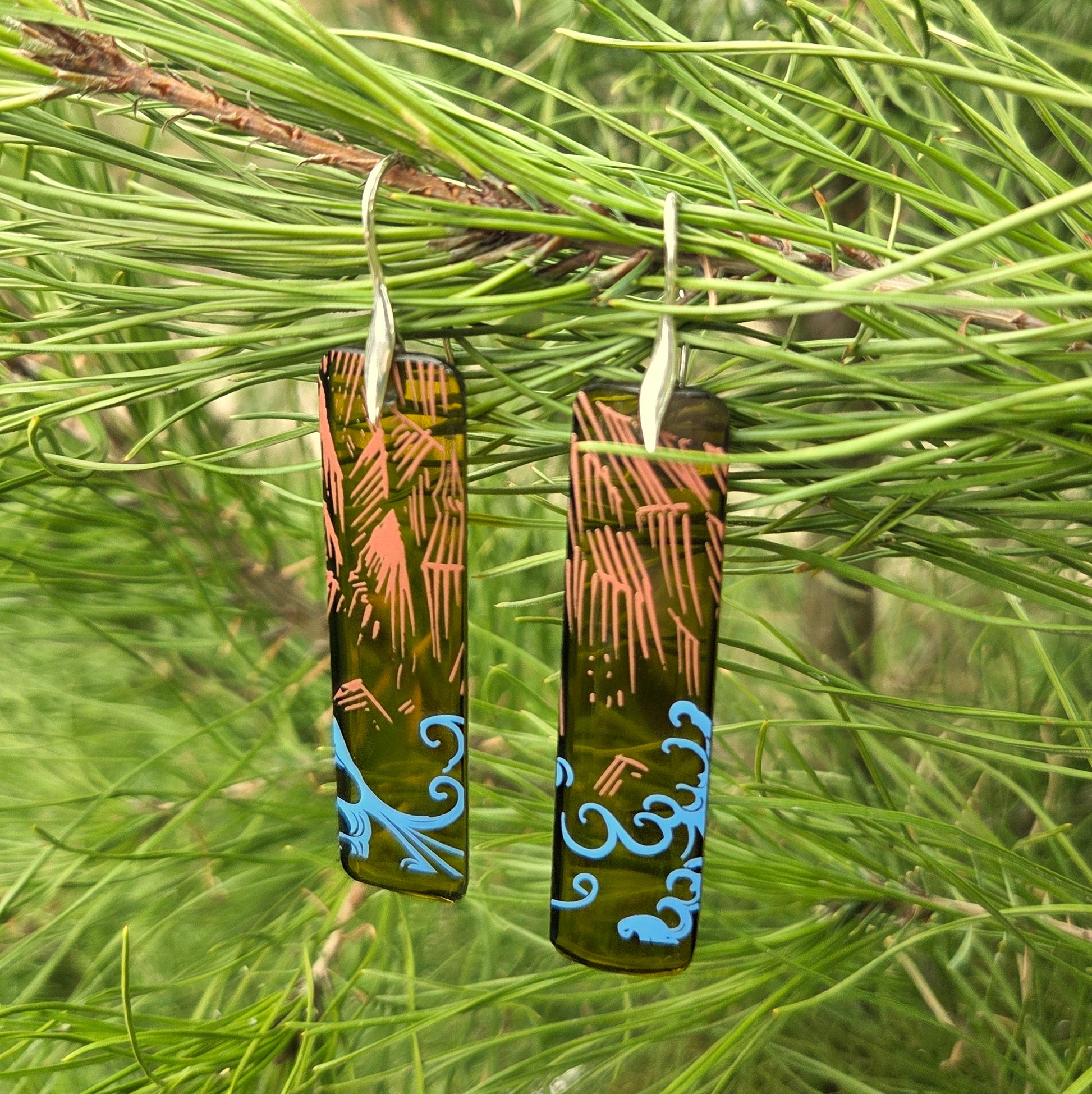 Pair of glass earrings with intricate designs hanging on a branch
