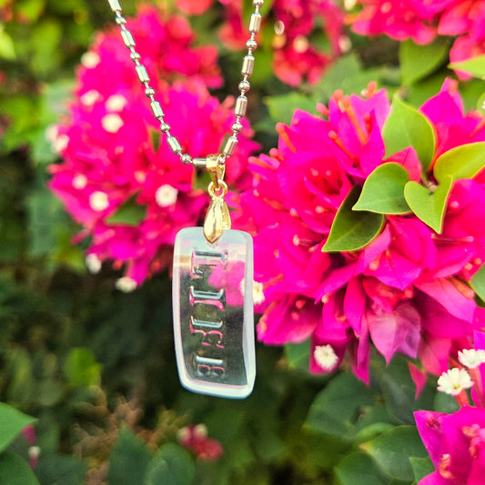Clear glass pendant saying "life" hanging from a silver/gold chain in front of pink florals.