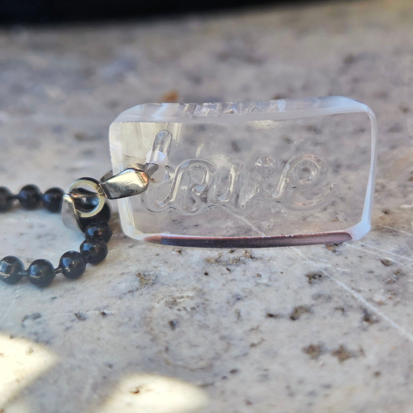 Clear glass pendant with love written on it, on black ball chain.