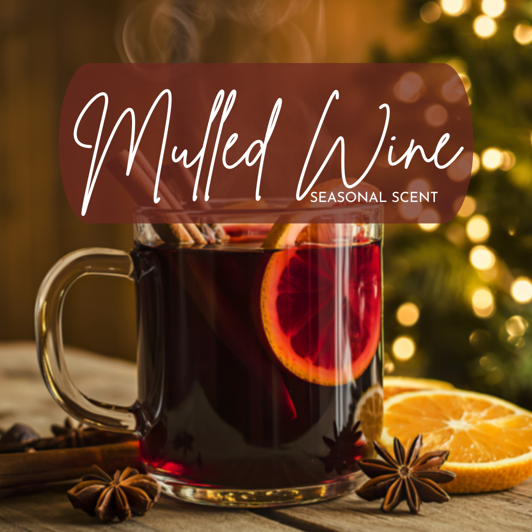 A cozy, holiday-inspired image featuring a clear glass mug filled with steaming mulled wine, garnished with a bright orange slice, cinnamon sticks, and star anise on a rustic wooden table. Warm golden bokeh lights and a softly blurred Christmas tree glow in the background, creating a festive winter atmosphere. Overlay text reads “Mulled Wine – Seasonal Scent,” evoking notes of spiced red wine, citrus peel, and cozy holiday warmth.
