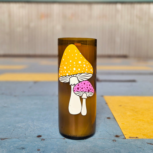 Front-facing view of a wine bottle candle made from recycled glass, featuring bold mushroom art in orange and magenta. The handmade candle blends charm and sustainability with a clean, modern design.