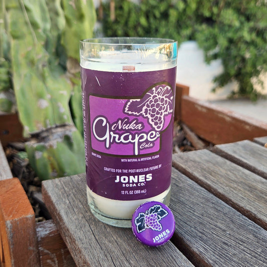 Jones Soda Nuka Grape bottle candle and cap on a wooden surface with greenery in the background