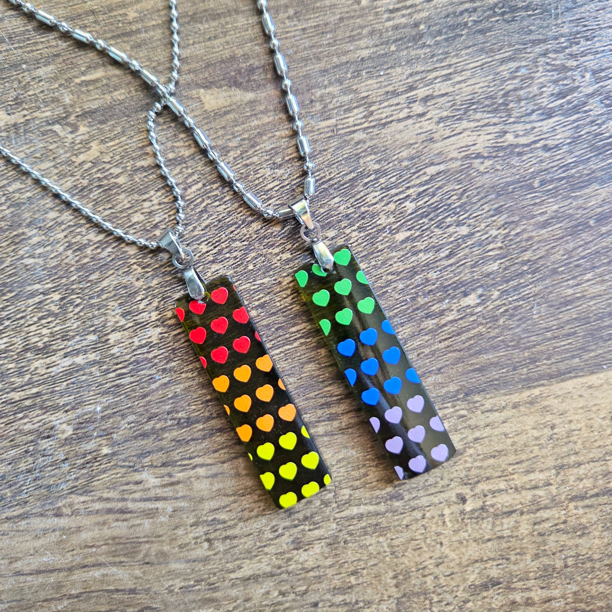 Two necklaces with colorful heart patterns on a wooden surface