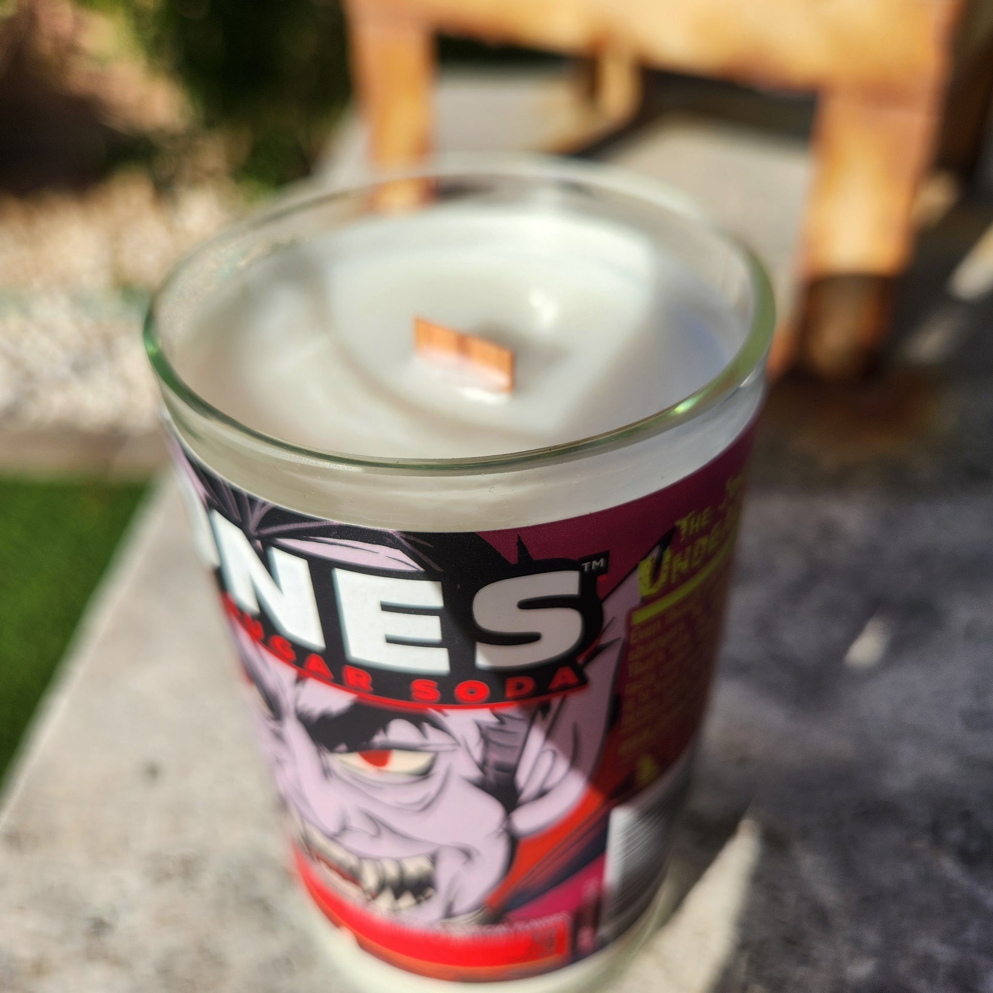 A close-up of a coconut soy wax candle in a recycled bottle with a smooth glass rim and wooden wick; the label displays a cartoon vampire face and bold “JONES” text, creating a playful spooky vibe for this eco-friendly wine bottle candle.