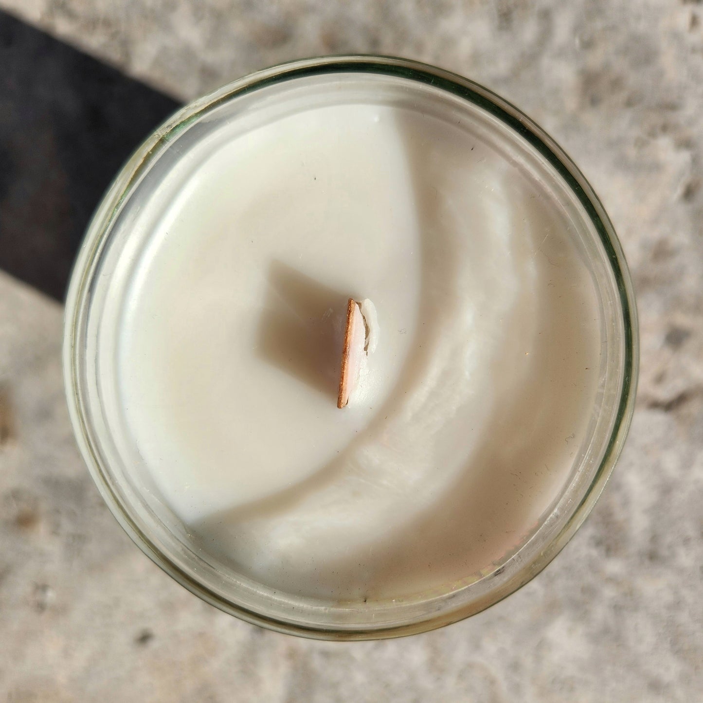 A direct top view of an unlit coconut soy wine bottle candle with a wooden wick centered in smooth white wax, housed in a recycled bottle with clean edges and a faint green tint to the glass.