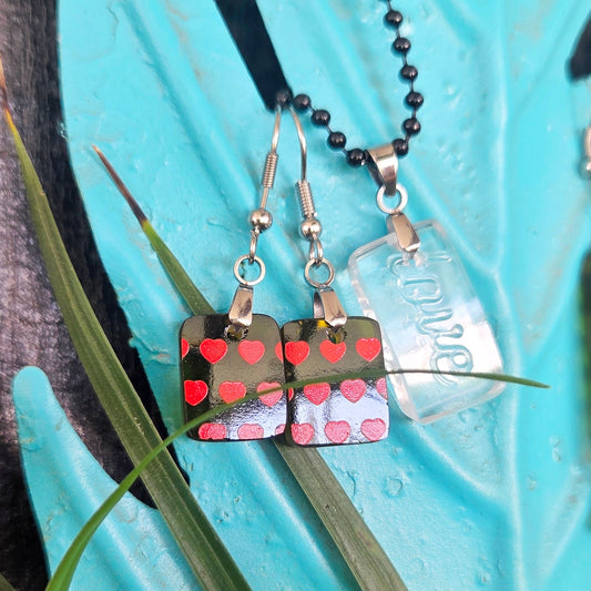Pair of glass earrings with a red heart design  and pendant with raised letter spelling love on a light blue background