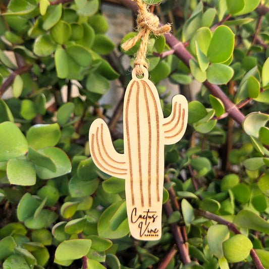 Reusable, Wooden cactus shaped air freshener hanging on a branch with green leaves.