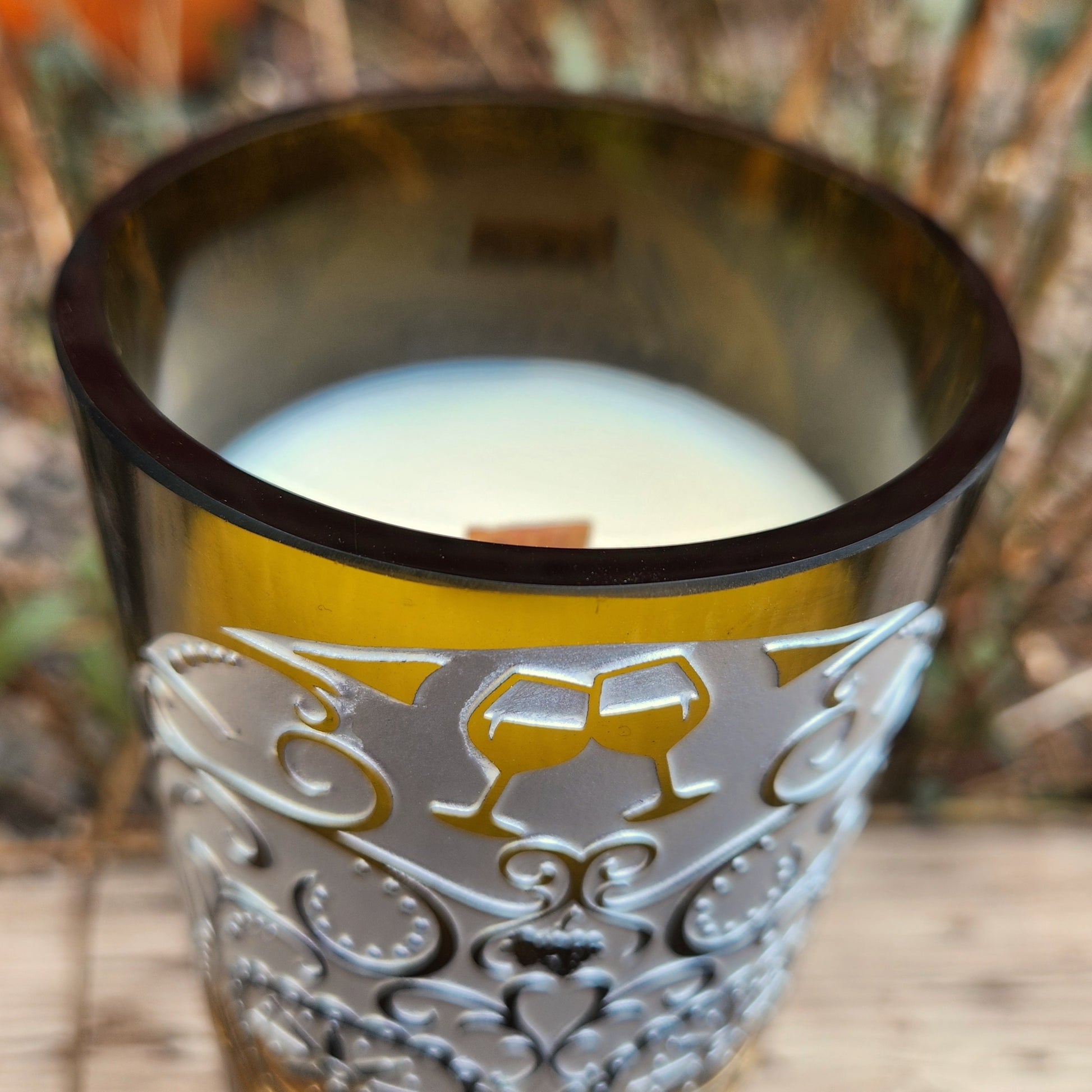Close-up of a handmade wine bottle candle with a glossy smooth rim, wooden wick, and elegant sugar skull and filigree etching, made from a recycled wine bottle.