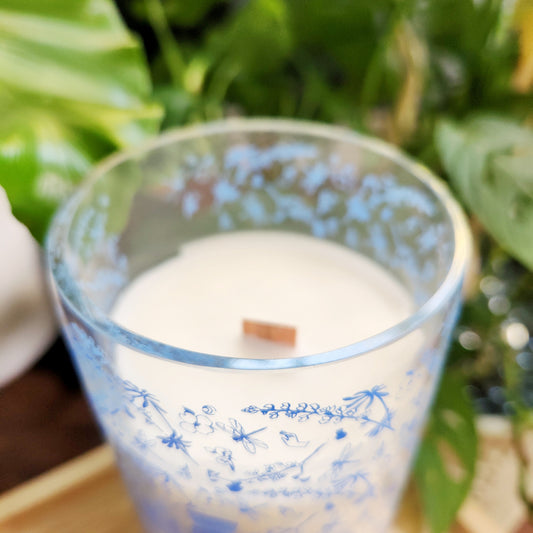 Close-up of a coconut soy wax wine bottle candle with intricate blue floral detailing around the rim. The wooden wick sits neatly in the creamy, non-toxic wax, highlighting the candle’s clean, sustainable burn and handmade craftsmanship.