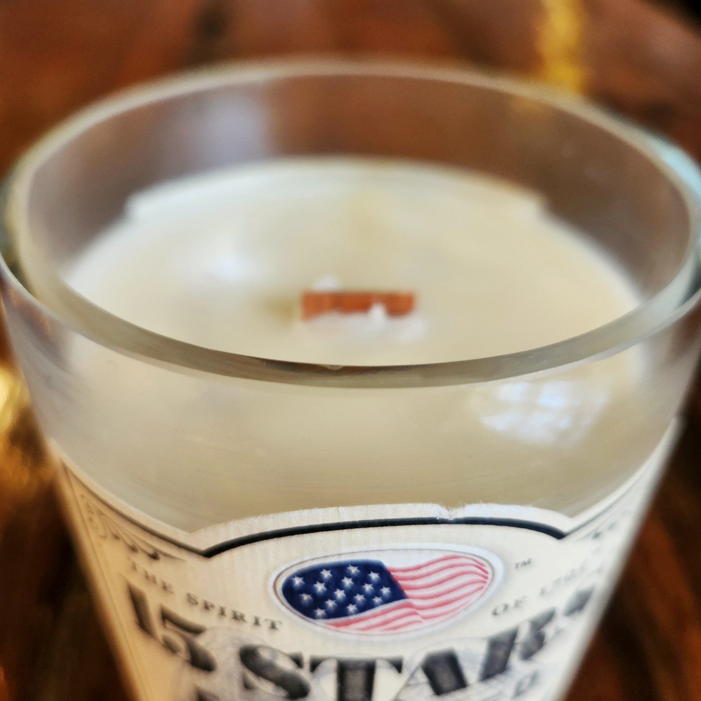 Close-up of a sustainable candle's smooth rim and wooden wick inside a repurposed 15 Stars rye whiskey bottle, featuring creamy white wax