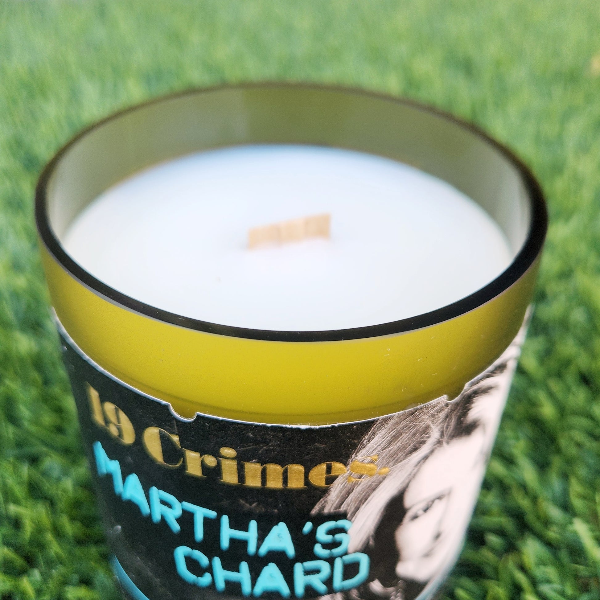 Close-up of the shiny, smooth glass rim on a recycled wine bottle candle labeled "Martha's Chard." The clean-cut rim frames the creamy coconut soy wax and wooden wick, highlighting craftsmanship and sustainability.