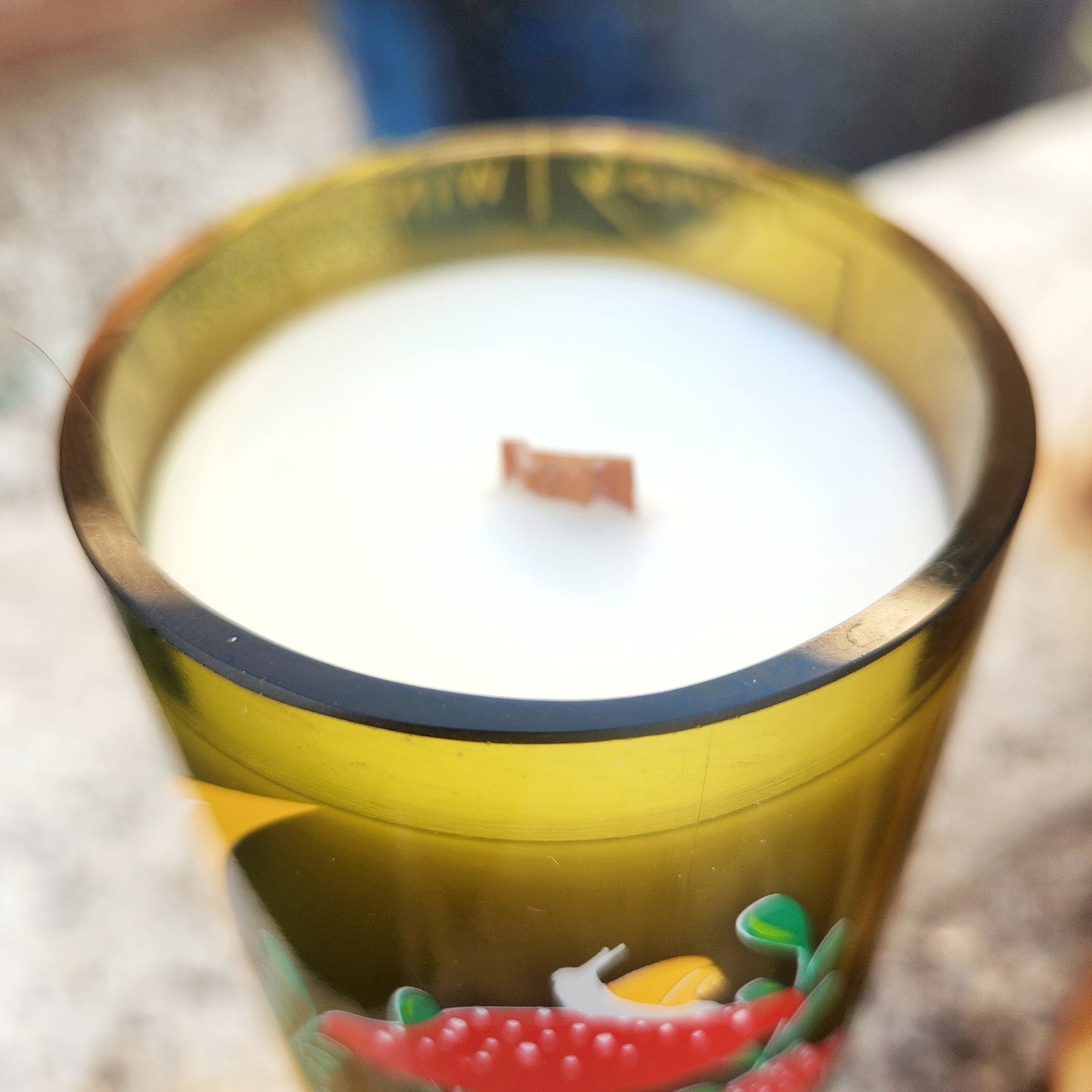 Close-up of a mushroom moon-themed candle with a crisp wooden wick and creamy white coconut soy wax. The shiny cut edge of the recycled wine bottle reflects golden tones in the light, emphasizing its handcrafted, upcycled charm.