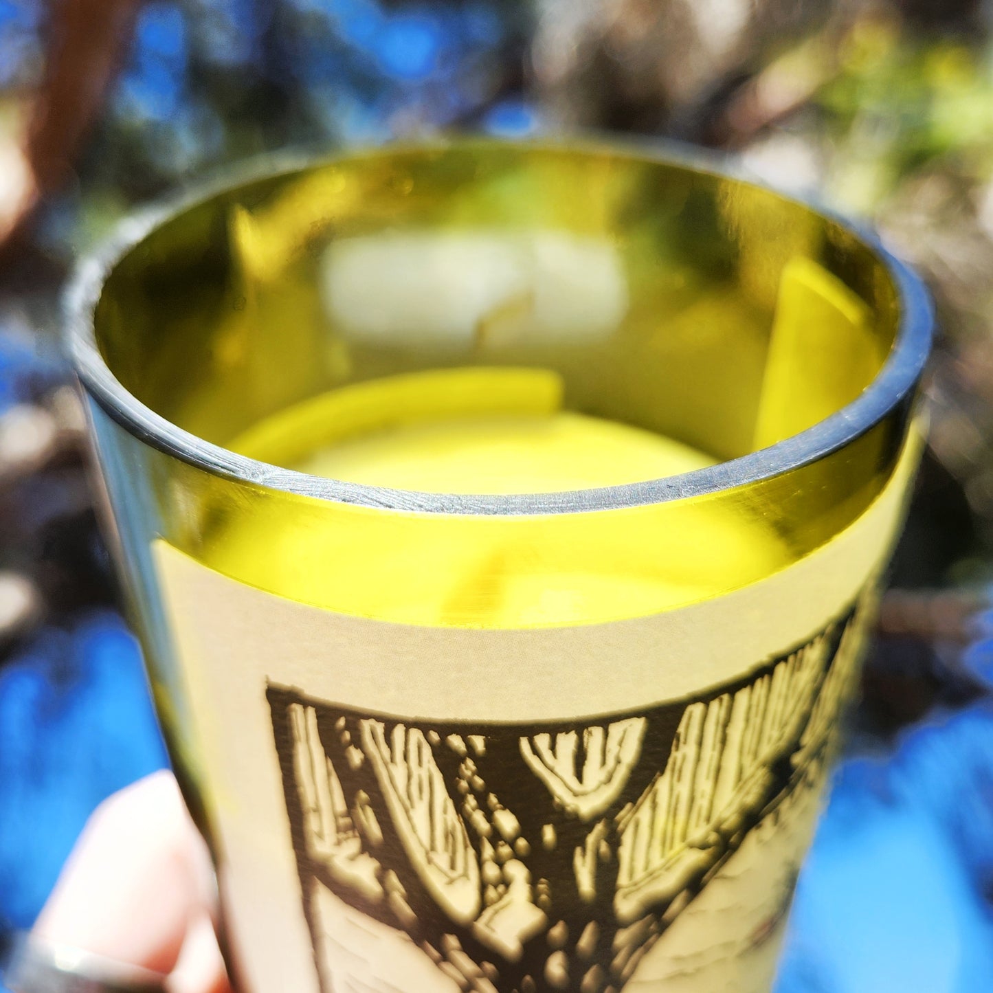 Close-up of the smooth-cut rim and partial label on a Red Sled wine bottle candle, highlighting the polished edge and golden green glass of this upcycled, eco-friendly candle.