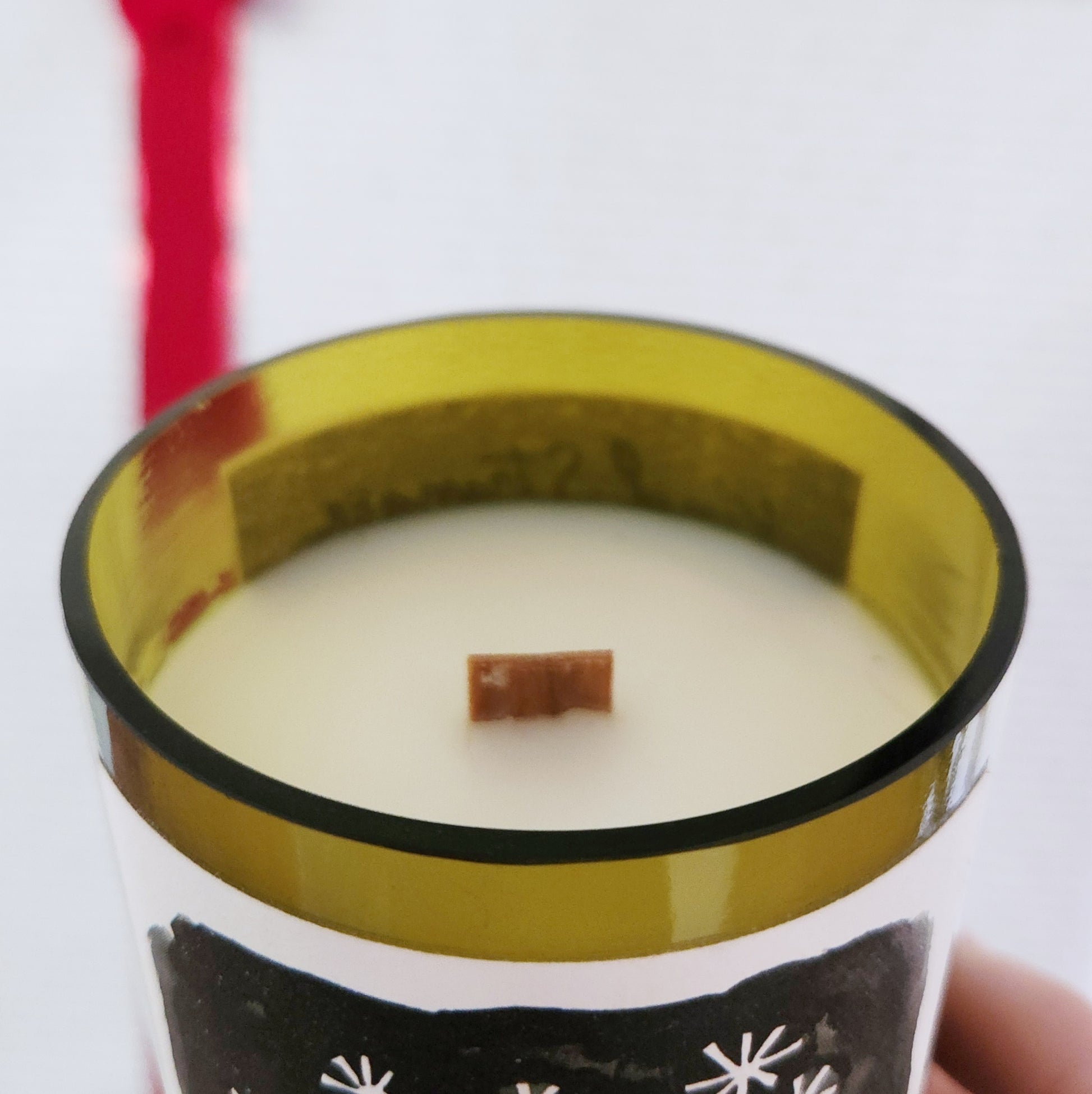 Close-up of a clean-burning, hand-poured wine bottle candle made with eco-friendly coconut soy wax and a wooden wick, housed in a recycled green wine bottle with a smooth glass rim and partial winter-themed label visible.