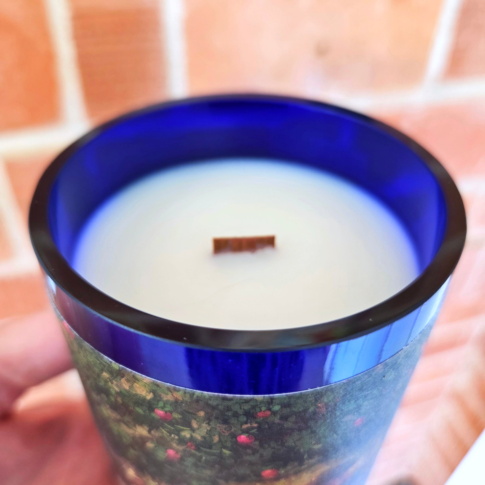 Close-up view of a hand-poured wine bottle candle with a vibrant blue rim, smooth glass edge, and wooden wick centered in creamy coconut soy wax, highlighting the clean, eco-friendly craftsmanship.
