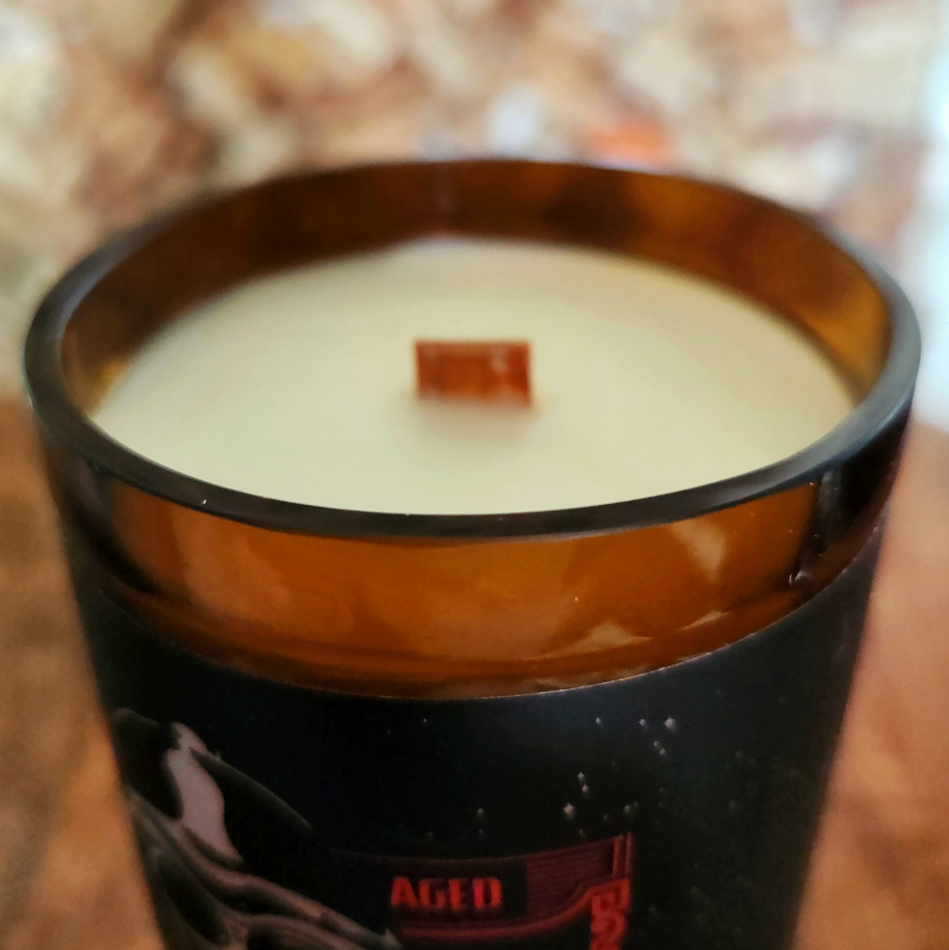 A zoomed-in shot of a hand-poured coconut soy candle with a wooden wick inside a recycled beer bottle. The smooth, shiny glass rim highlights the upcycled craftsmanship and clean-burning eco-friendly materials.
