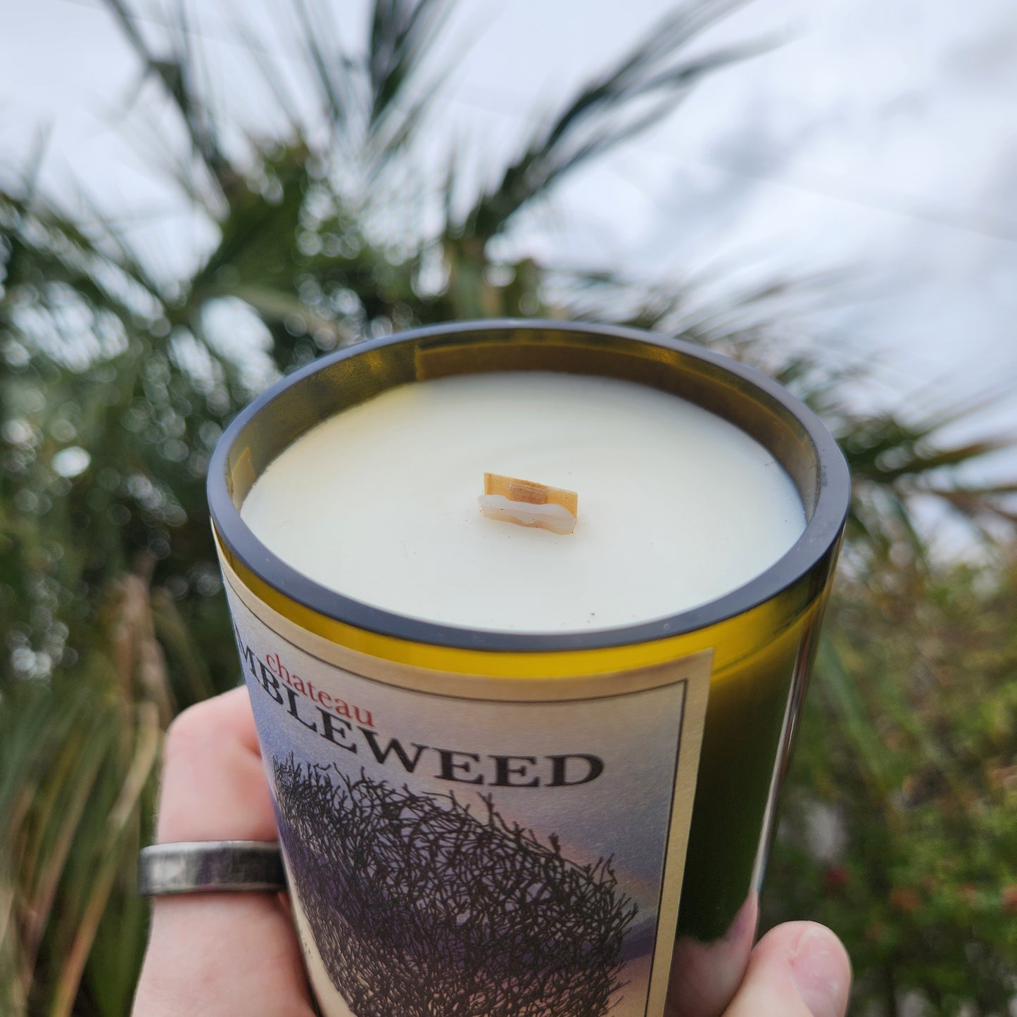 Close-up angled view of a wooden wick candle in a recycled Chateau Tumbleweed wine bottle. The coconut soy wax has a creamy finish, and the smooth glass edge highlights the handmade charm.

