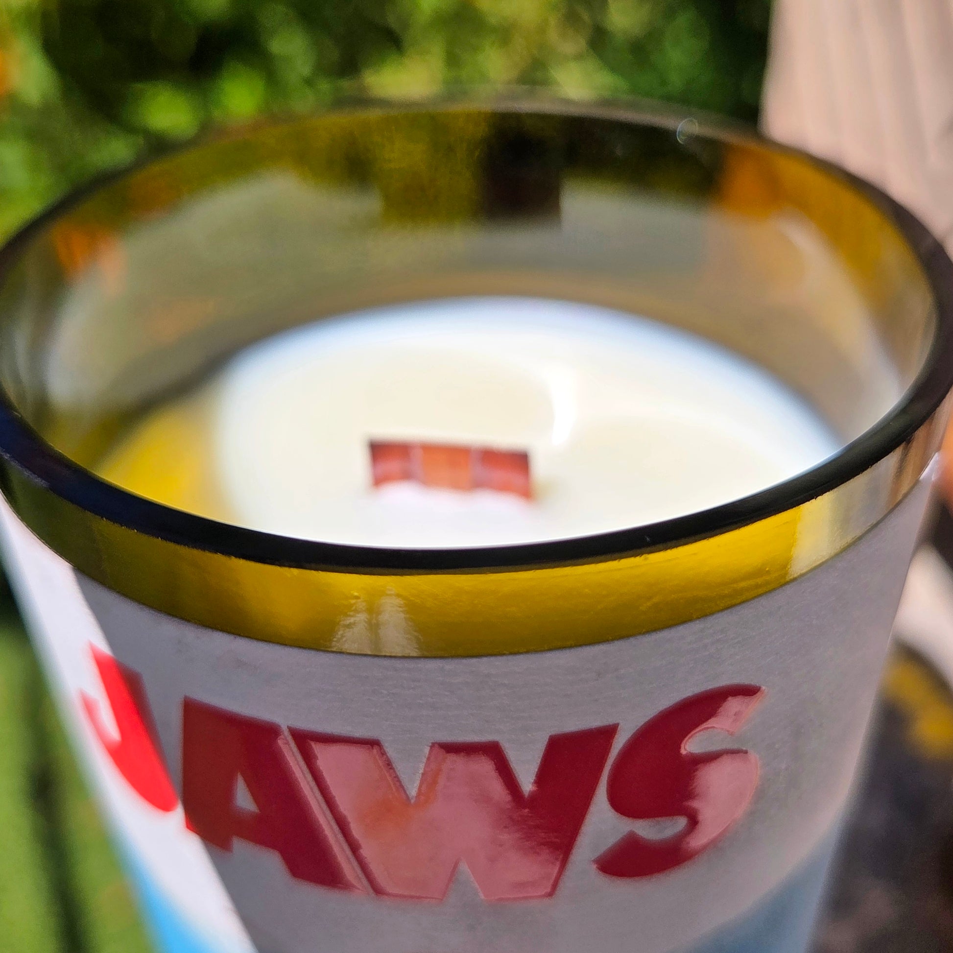 Close-up of a Jaws inspired wine bottle candle rim with shiny smooth glass, showing creamy coconut soy wax and a centered wooden wick inside the upcycled vessel.