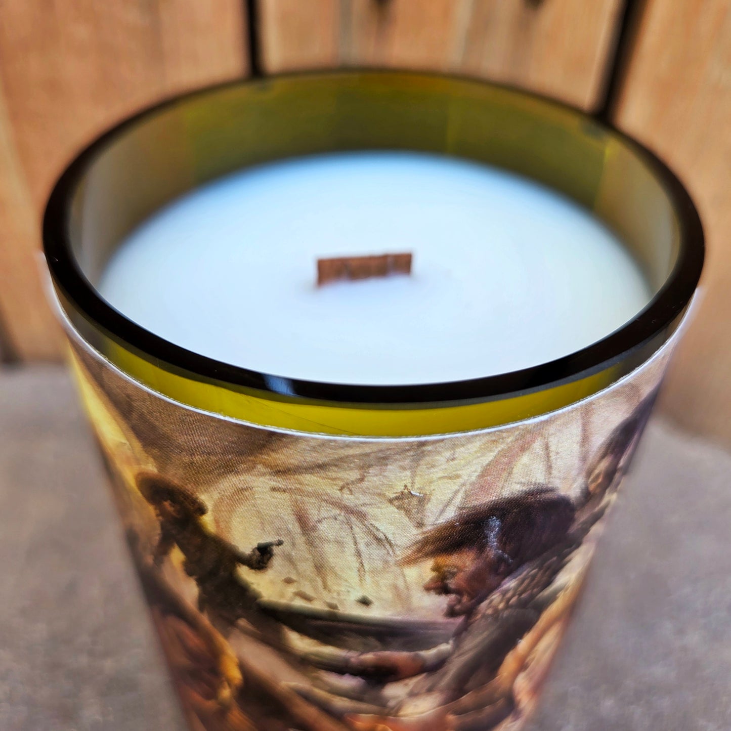 Close-up of the shiny, smooth glass rim of a wine bottle candle wrapped in vivid saloon shootout artwork. Hand-poured coconut soy wax and a wooden wick create a sustainable, clean-burning candle.