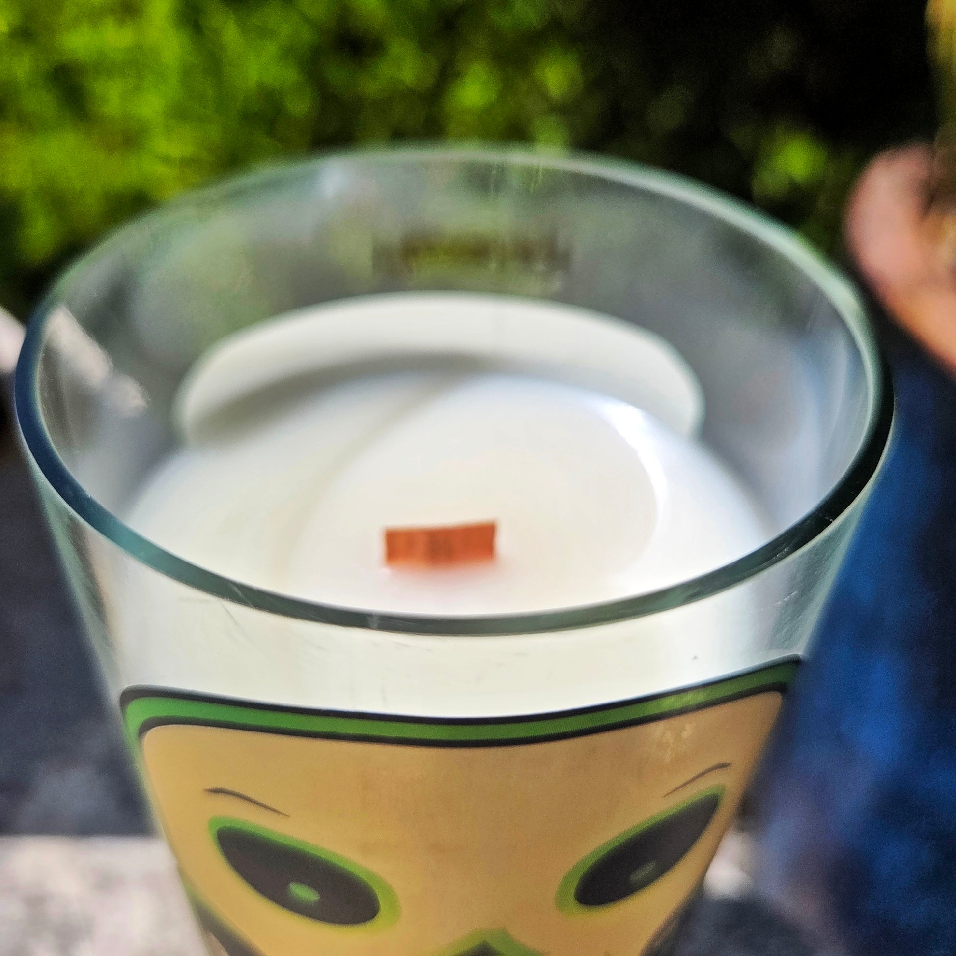 Close-up of the shiny smooth rim of a Spooky Juice wine bottle candle, showing creamy white coconut soy wax and a centered wooden wick inside the upcycled glass ves
