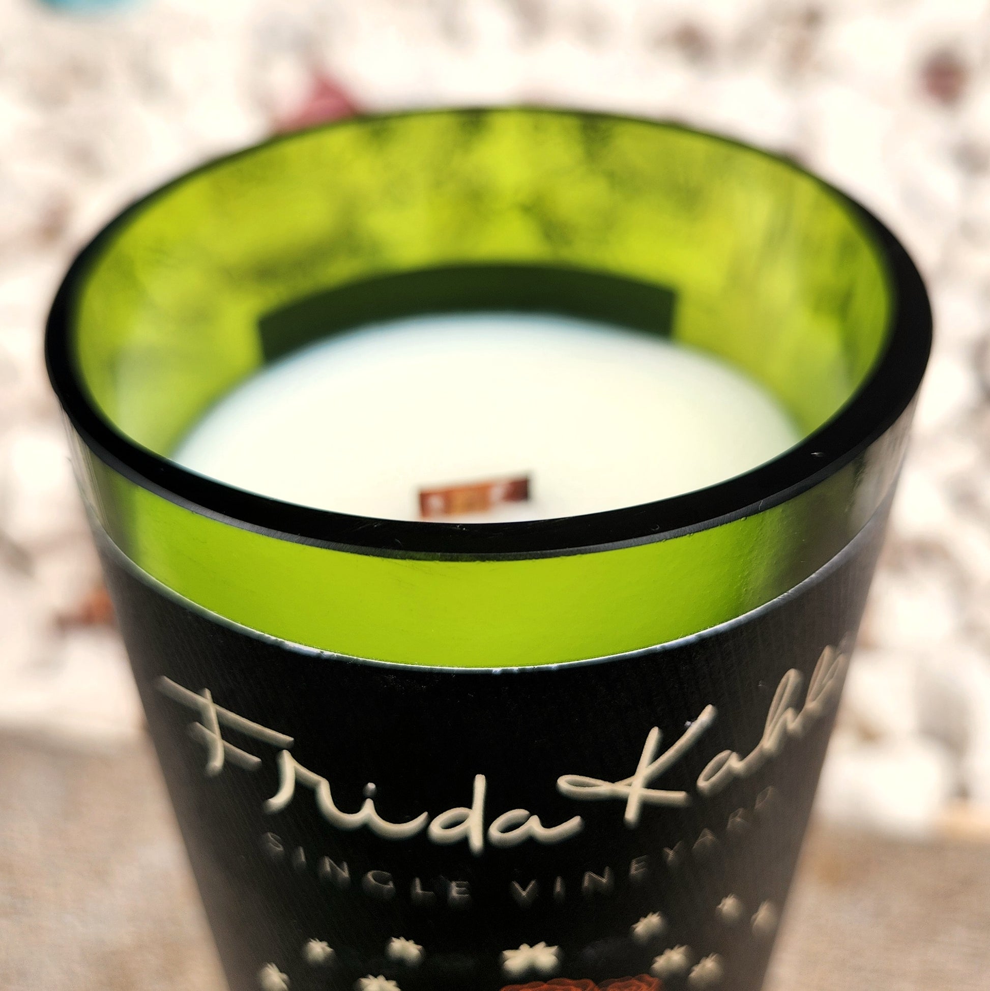 Close-up of the wooden wick and smooth rim of a repurposed Frida Kahlo wine bottle candle, showcasing the vibrant green interior and eco-friendly coconut soy wax pour.

