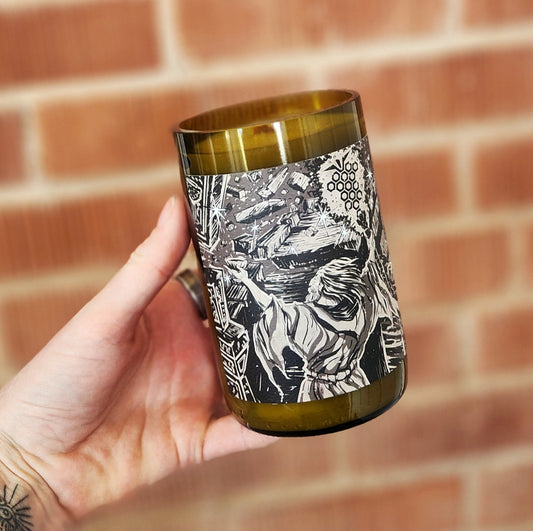 A hand-poured coconut soy wine bottle candle, featuring a detailed black-and-white rune-inspired illustration of a mystical figure casting energy in a cosmic scene. The eco-friendly wine bottle candle has a smooth, polished rim and a wooden wick for a clean, crackling burn. It is held in front of a red brick wall.