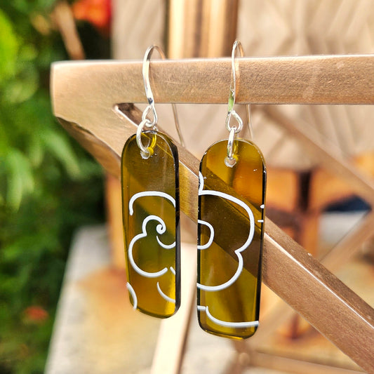 Pair of amber glass earrings with white cloud patterns hanging on a metal surface.