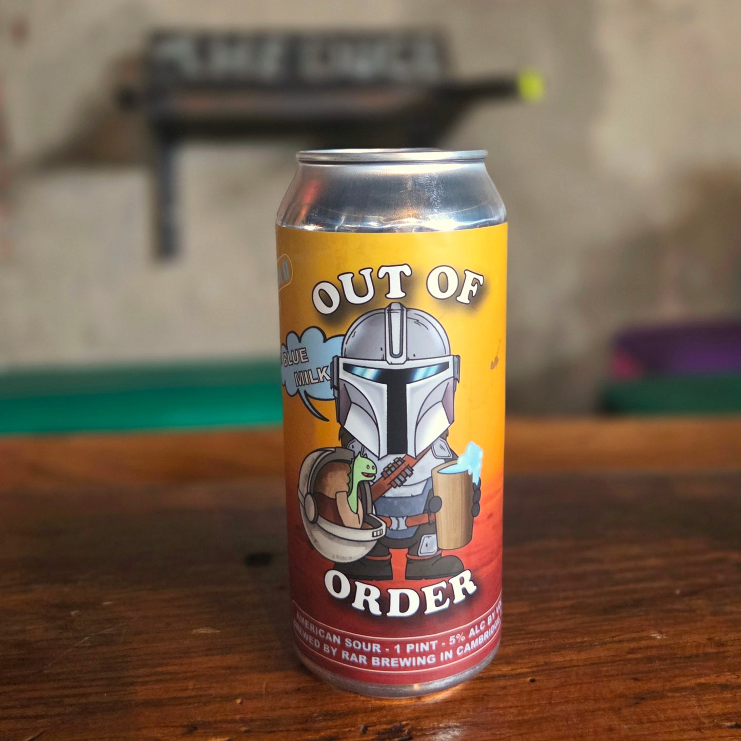 A hand-poured beer can candle made from a recycled "Out of Order" sour ale can featuring a Mandalorian-inspired character holding a mug of blue milk, with a baby alien companion in a floating pod. This eco-friendly wooden wick candle brings a playful, galactic vibe to your space—perfect for Star Wars fans and collectors.