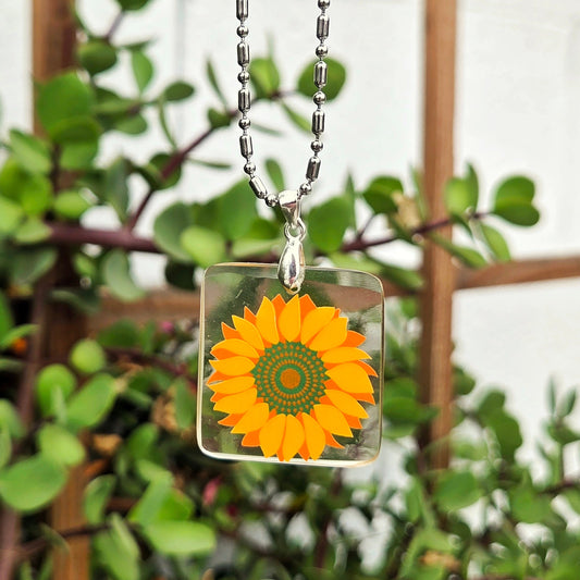 Necklace with a sunflower pendant against a green foliage background