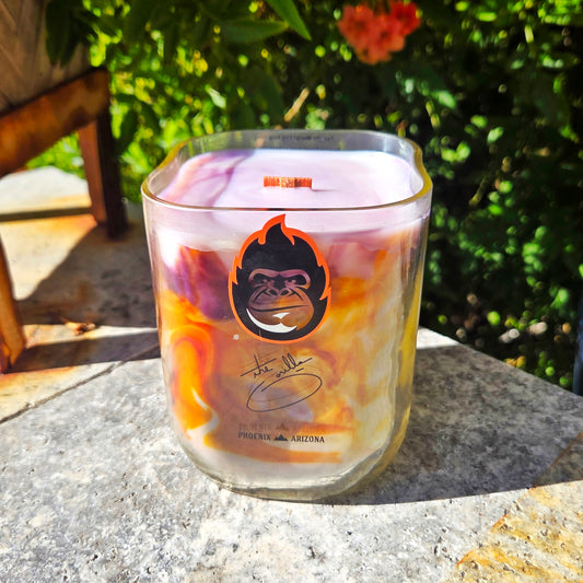 Candle in a glass container with a logo on a stone surface outdoors