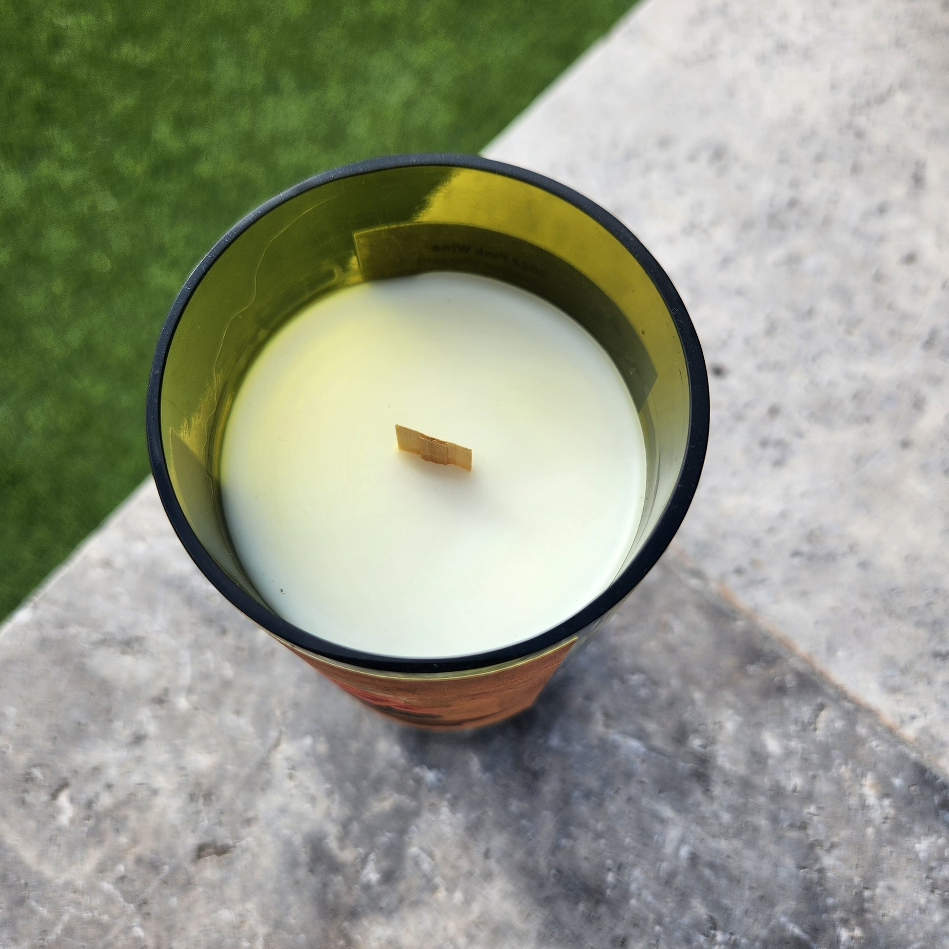 Top-down view of a hand-poured coconut soy candle in a recycled Dos Cabezas wine bottle, featuring a clean white wax surface and centered wooden wick. The smooth, curved rim of the upcycled glass glows softly in the sunlight, showcasing the eco-friendly craftsmanship and artisanal charm of this Arizona-made wine bottle candle.