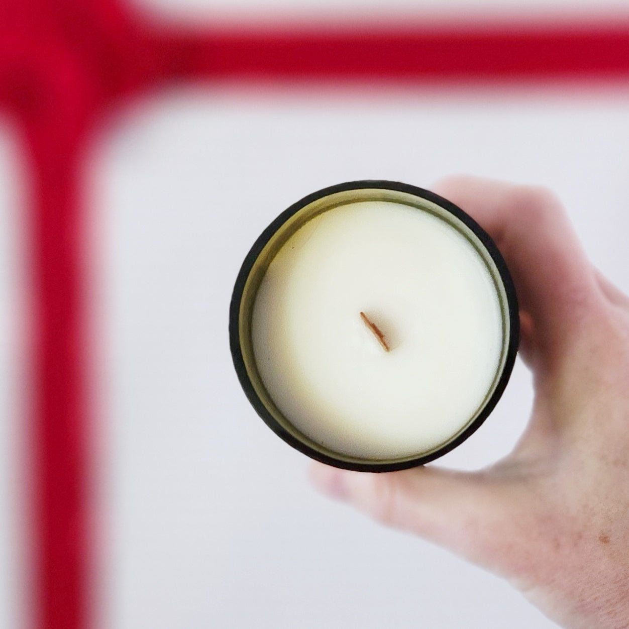 Top-down view of a creamy white coconut soy wax wine bottle candle with a centered wooden wick, poured into a glossy, upcycled wine bottle vessel, held in hand against a bright background.