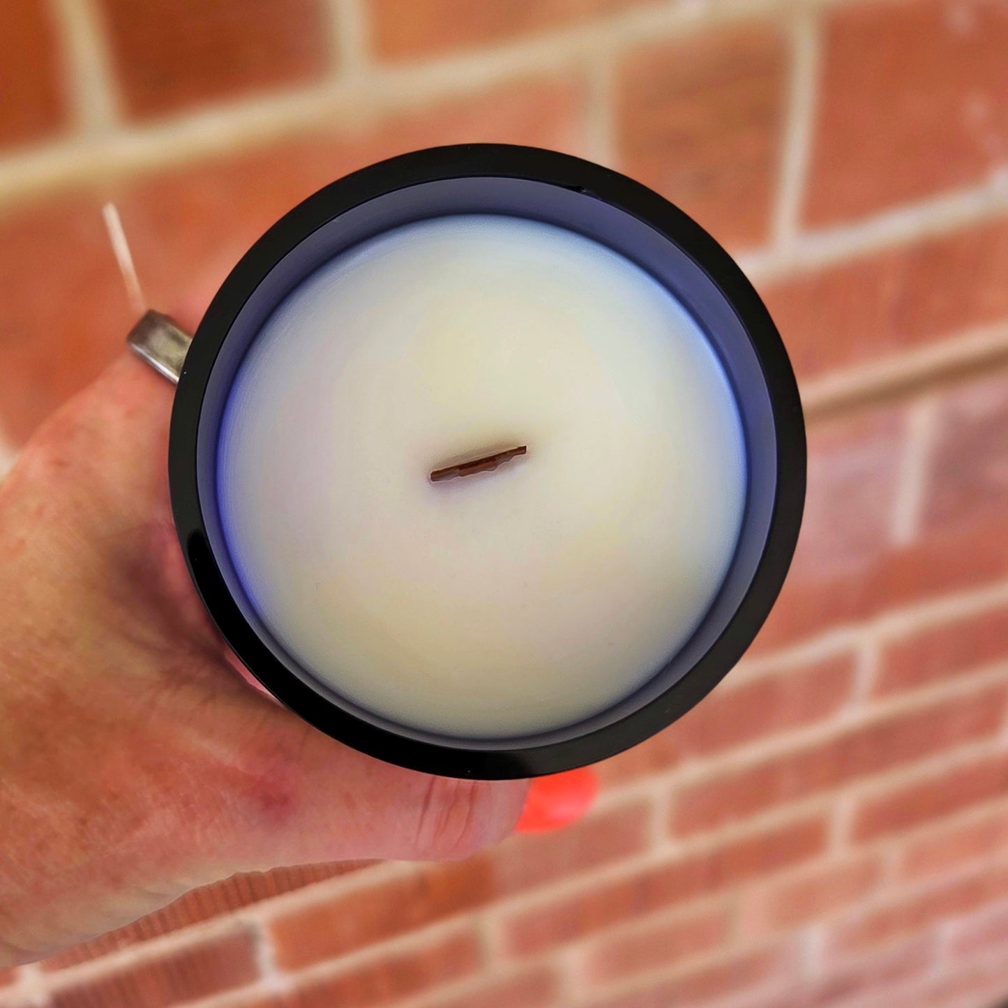 Top view of a clean-burning wine bottle candle with white coconut soy wax and centered wooden wick, housed in a dark blue recycled bottle with a polished, smooth rim.