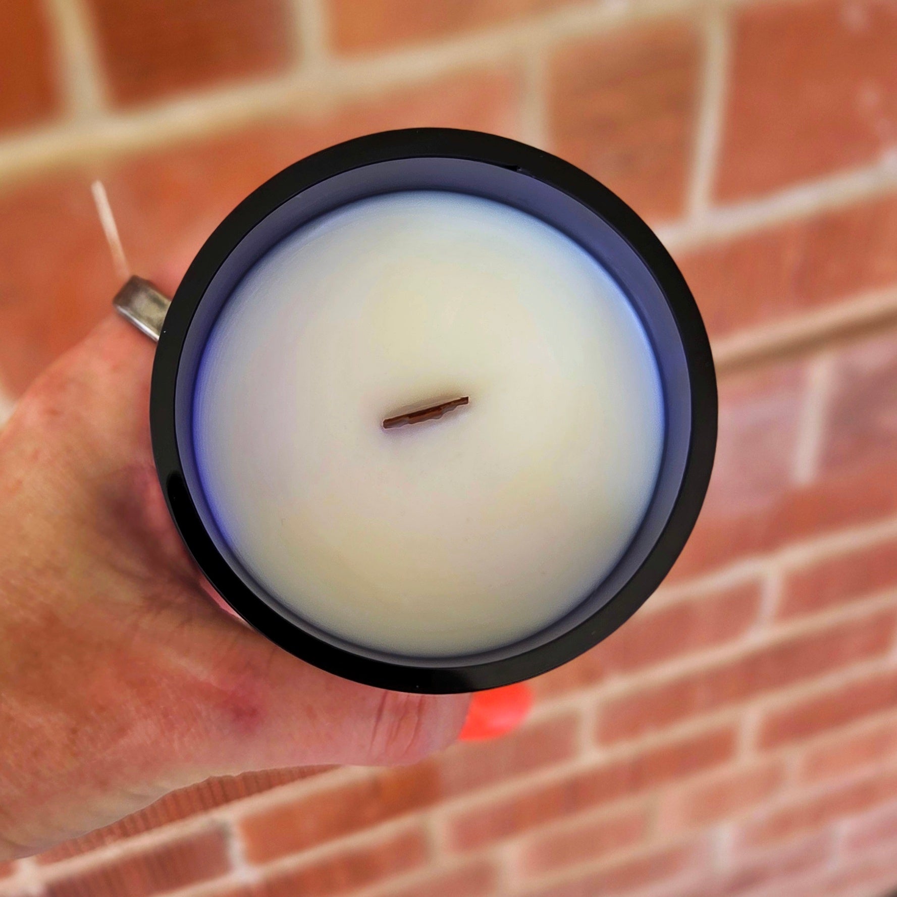 Top view of a clean-burning wine bottle candle with white coconut soy wax and centered wooden wick, housed in a dark blue recycled bottle with a polished, smooth rim.