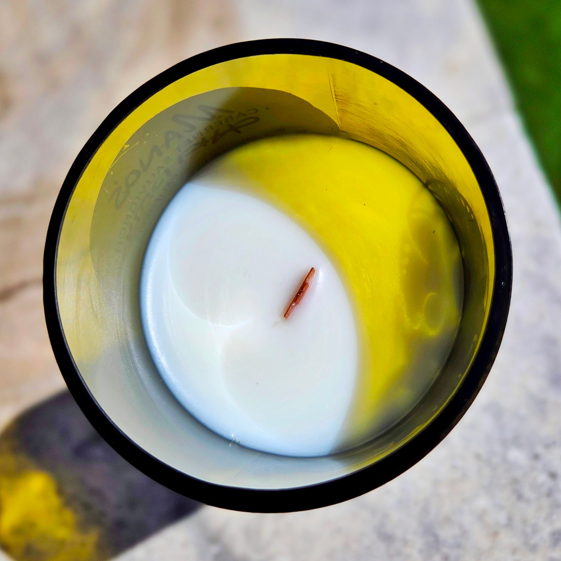 Top-down view of a hand-poured coconut soy wax wine bottle candle with a crackling wooden wick, housed in a recycled bottle with a smooth glass rim and faint yellow tint, highlighting the clean eco-friendly burn.