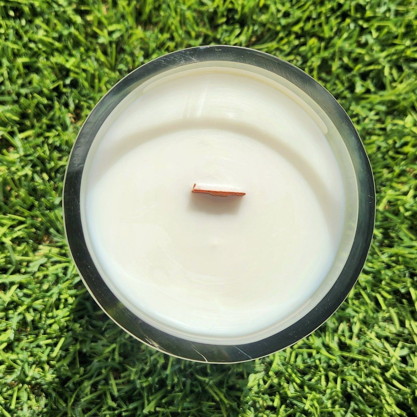 Overhead view of a hand-poured August candle, highlighting the eco-friendly wooden wick and glossy white wax inside a recycled wine bottle vessel with a gently curved rim.

