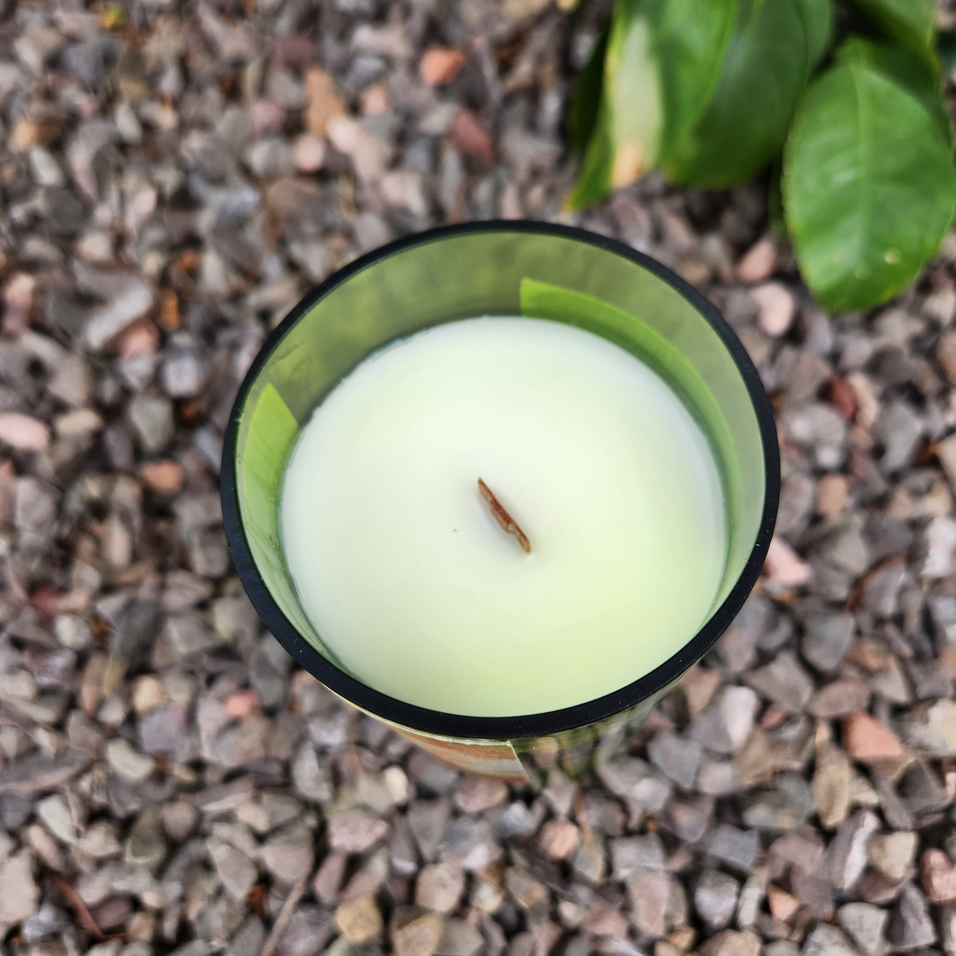 Top view of a clean-burning wine bottle candle with coconut soy wax and a wooden wick inside a green upcycled wine bottle. The gravel background and soft wax texture emphasize the candle’s handmade charm.