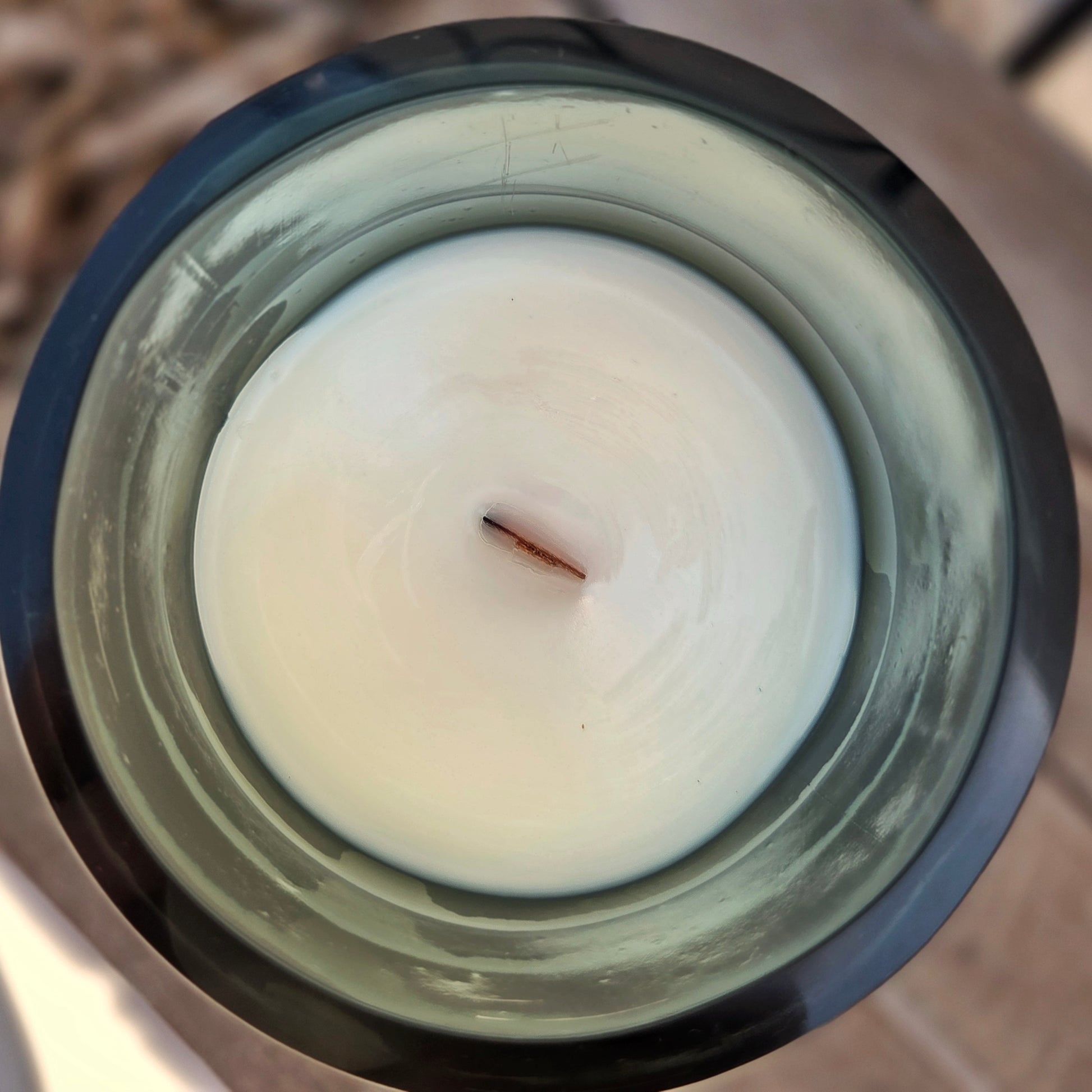 Top-down view of a handmade wine bottle candle with smooth coconut soy wax and a wooden wick, highlighting the clean and modern finish inside the upcycled gold glass vessel.